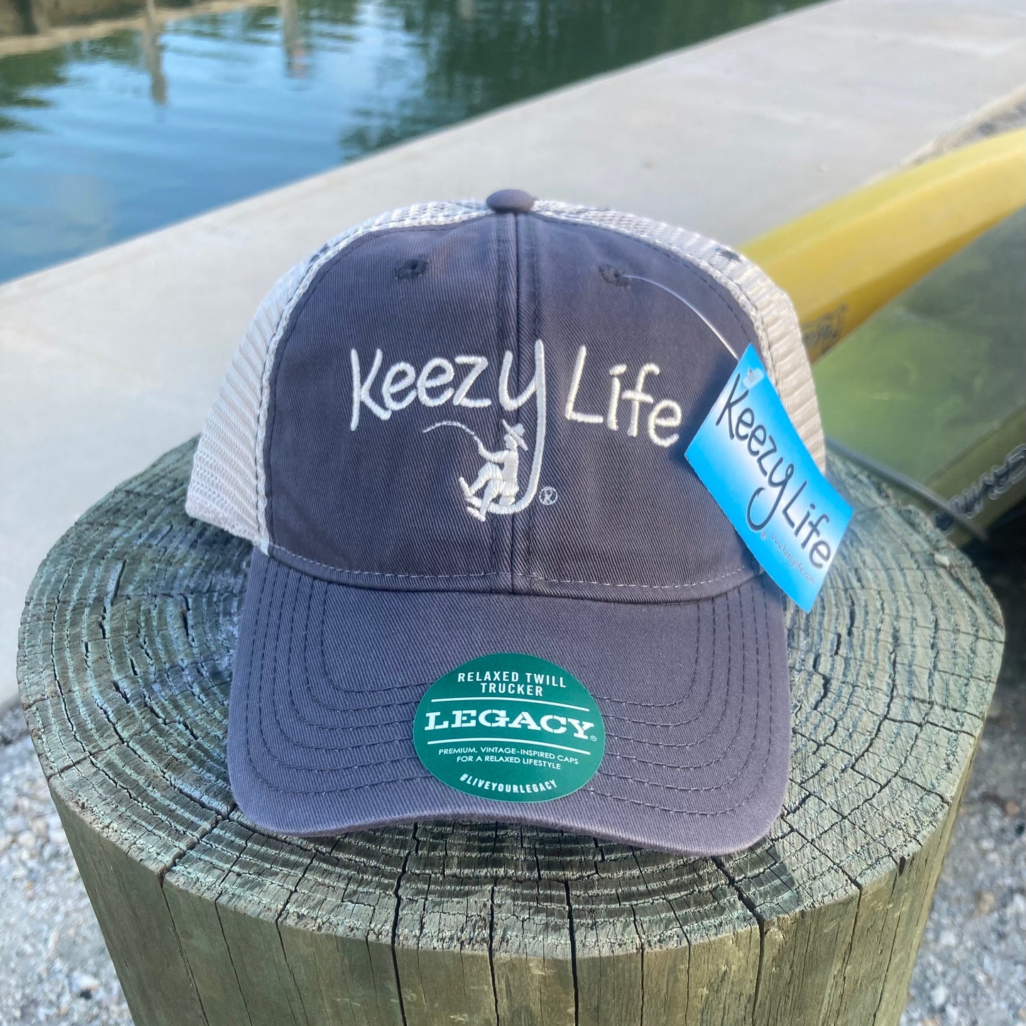 Grey trucker cap says Keezy Life. The letter Y has a boy fishing on the bottom of the Y.